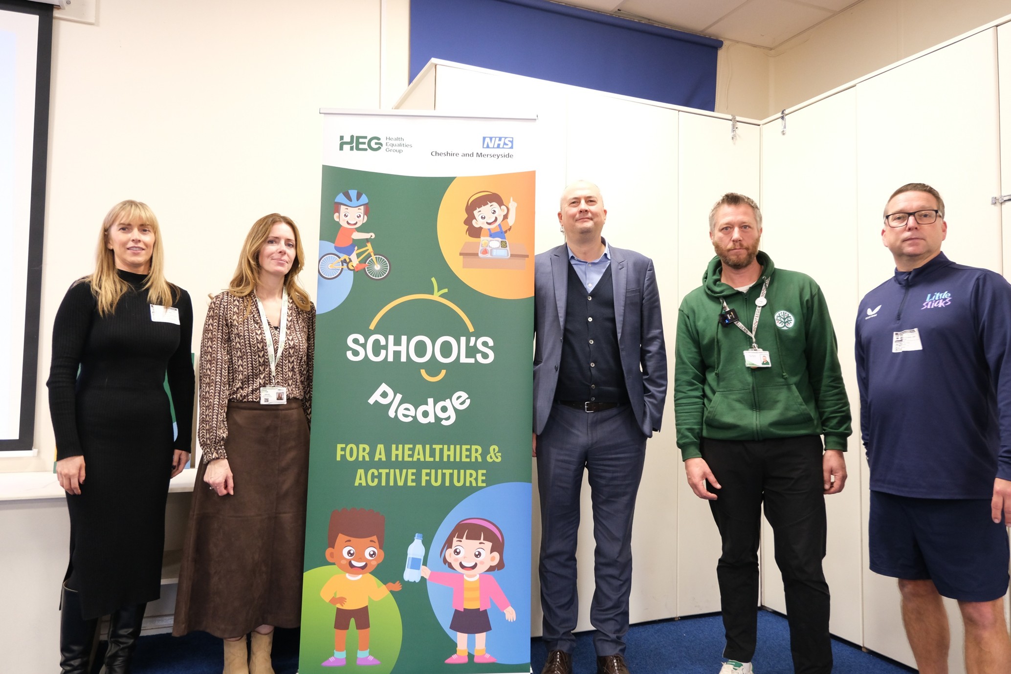Five people stand beside a colourful banner reading "School's Pledge: For a Healthier & Active Future."