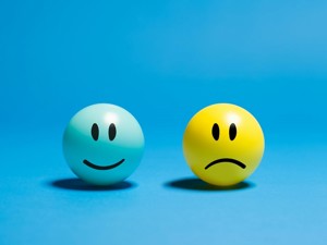 Two round balls on a blue background. The left ball is blue with a smiling face, and the right ball is yellow with a sad face, contrasting emotions.