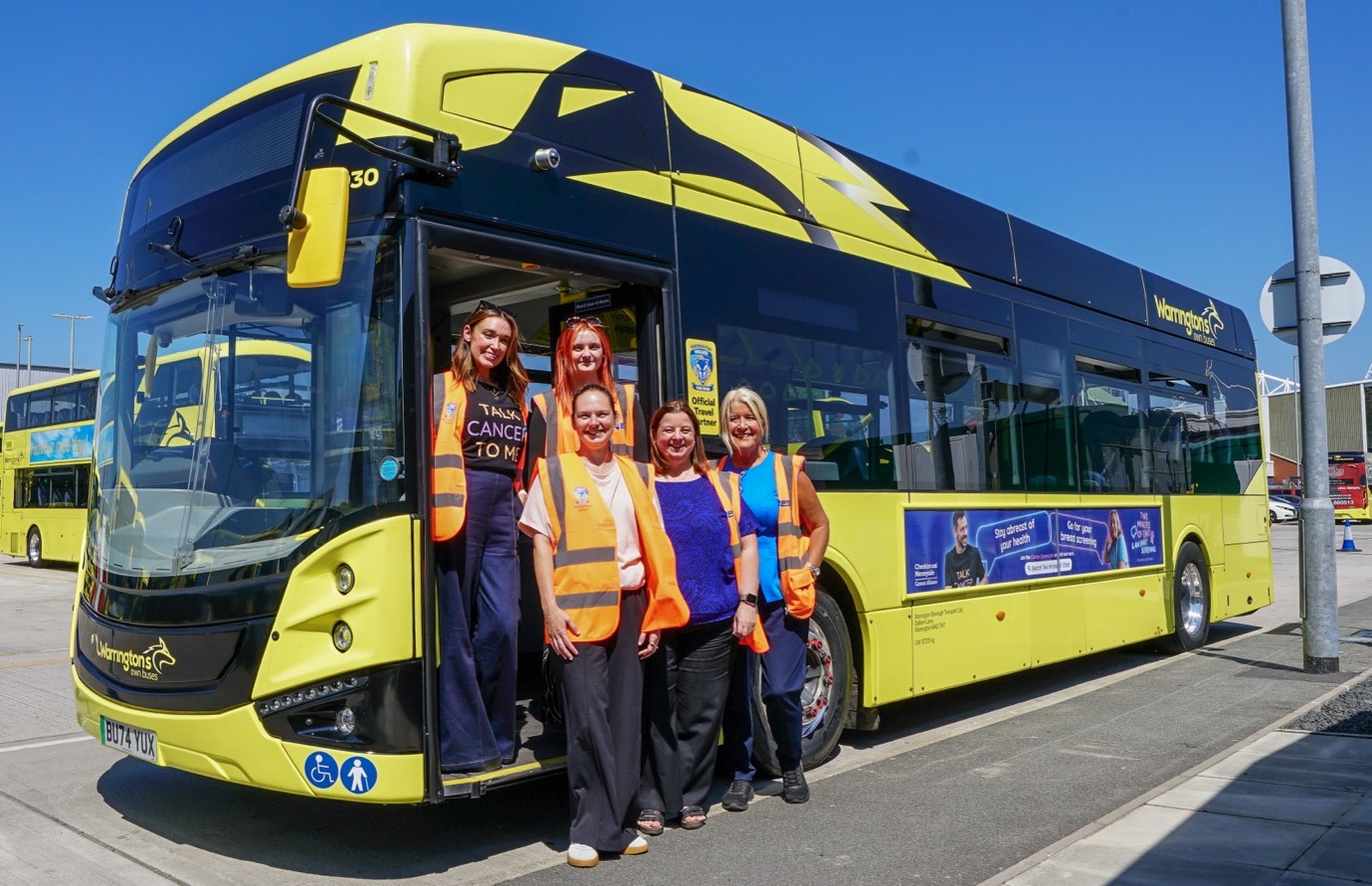 A group of five women standing in front of a yellow and black bus.