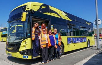 A group of five women standing in front of a yellow and black bus.